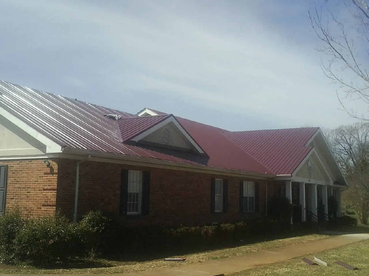 Red metal roof with gabled entries on a long brick building, from a Hail Damage Roof Repair job in Howell