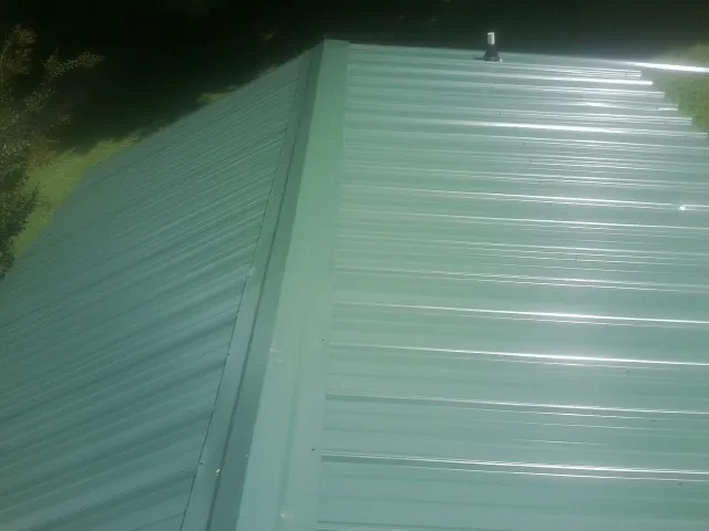 New green metal panels meeting at the ridge of a roof — Flat Roof Repair work by our crew in Howell