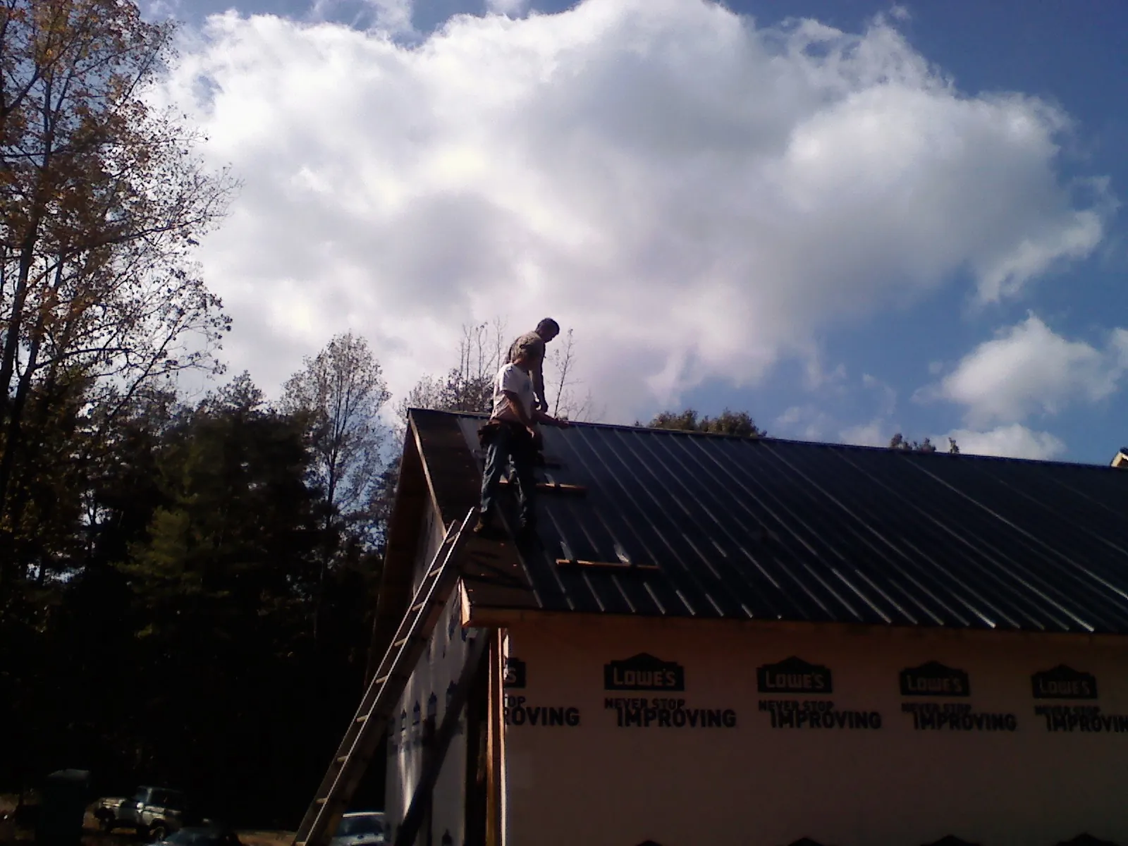 Roofer fastening dark metal panels high against a cloudy sky, from a Roof Inspection job in Howell