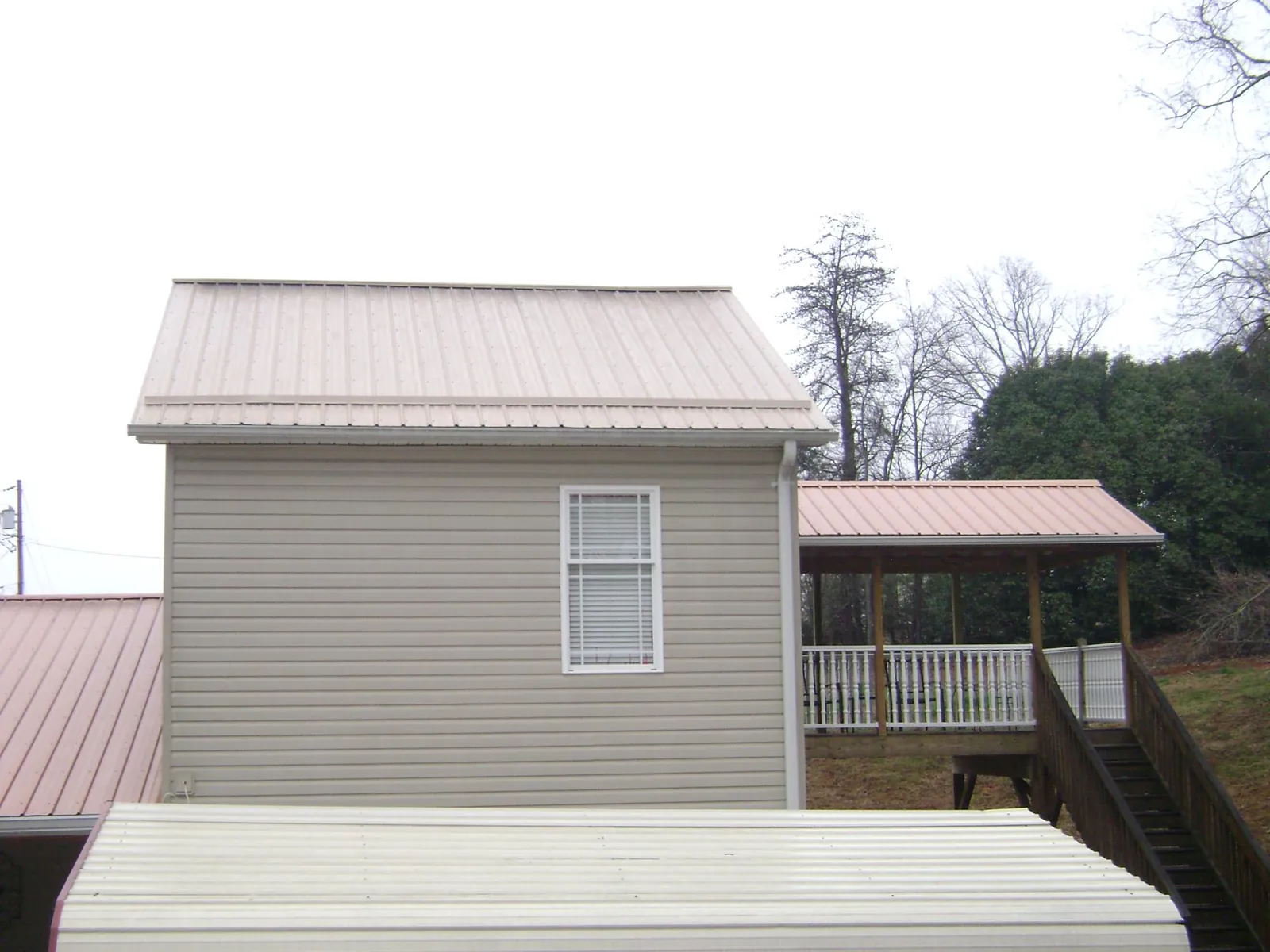 Tan metal roofs on a two story addition and attached porch, from a Roof Replacement job in Howell